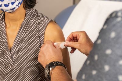 Ilustratīvs attēls, kurā sievietei plecā pēc vakcīnas saņemšanas uz injekcijas vietas līmē plāksteri